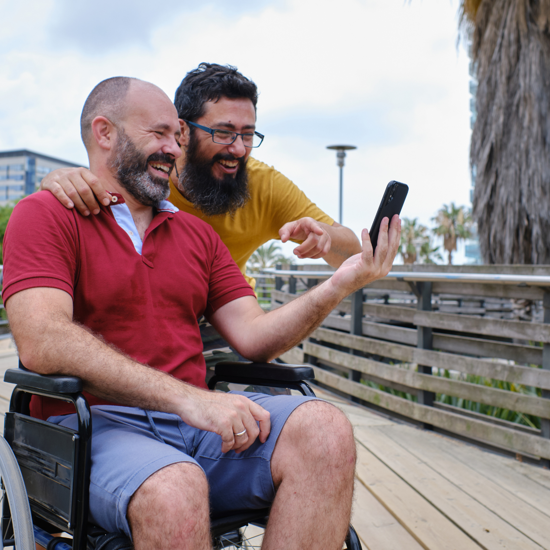 Male wearing a red t-shirt in a wheelchair and a male wearing a yellow t-shirt posing for a selfie