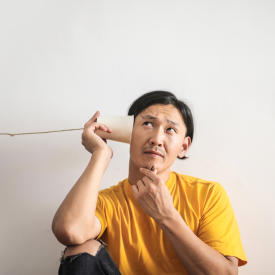 Male wearing a yellow t-shirt thinking with a pretend cup and string telephone