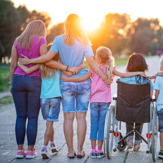 Two female adults and three female children with their arms around each other, one who is in a wheelchair