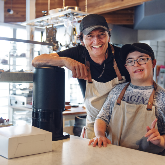 Male cafe owner with a young male with down syndrome working in a cafe