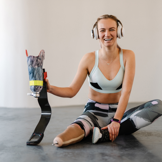 Female holding her prosthetic leg exercising with headphones on