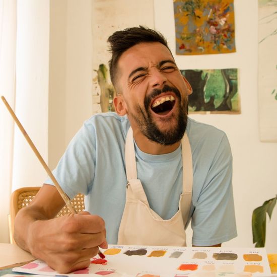 Male smiling whilst holding a paintbrush and painting