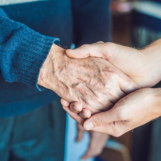 A close up of an elderly person holding hands with a caregiver