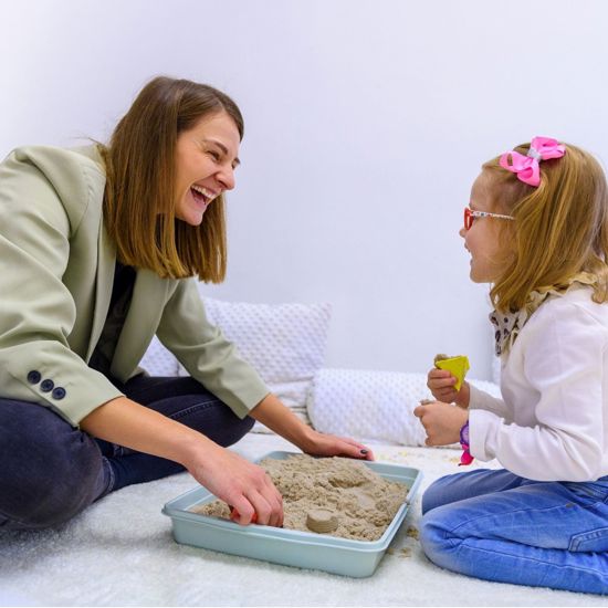 Female caregiver playing and laughing with a young girl wearing glasses